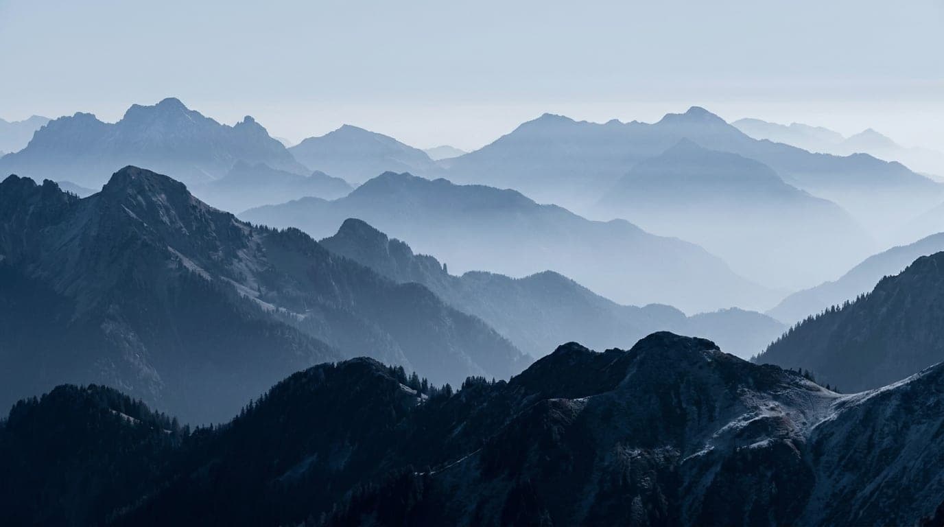 Kühle Alpenlandschaft in Blaustunden-Tönen: vielfach gestaffelte Bergketten, die sich in feinem Nebel verlieren.