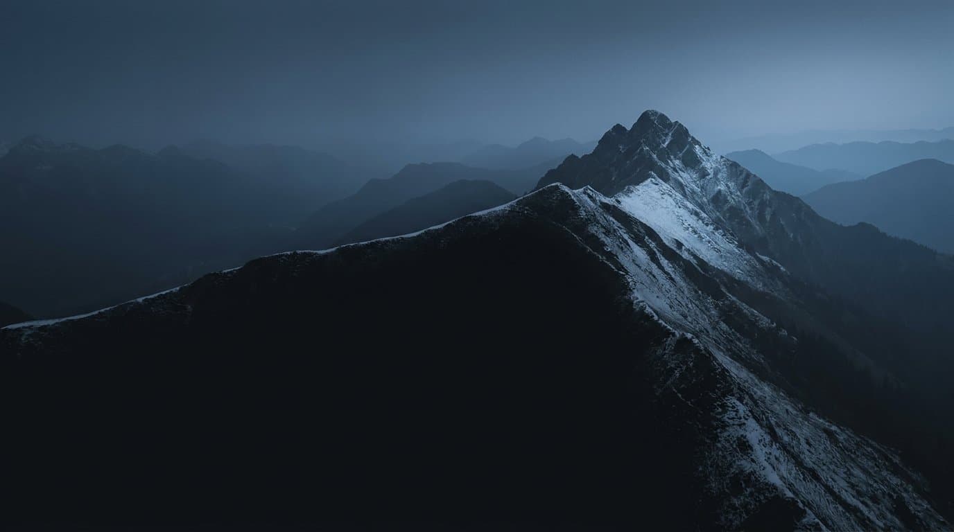 Kühle Alpenlandschaft zur blauen Stunde: ein Grat teilt die Szene in zwei ungleiche Hälften, die linke Flanke liegt im Schatten, die rechte fängt das letzte Schneelicht.